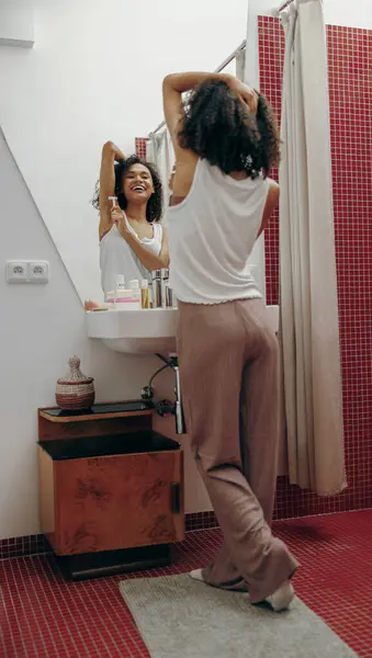 Positive woman shaving her armpits while looking at herself in the mirror in bathroom