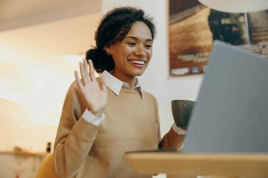 Young woman use laptop to make video call with friends and waving Hi while sitting at home clipart