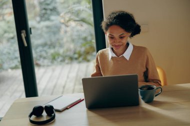 Dizüstü bilgisayarda çalışan serbest çalışan bir kadın uzaktan evde oturuyor ve başka tarafa bakıyor. Mesafe çalışma kavramı