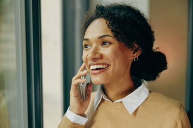 Ofisten çalışırken cep telefonuyla konuşan gülümseyen bayan girişimci.