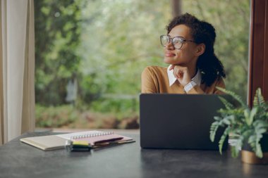 Evde otururken uzaktan bilgisayarla çalışan serbest çalışan bir kadın. Mesafe çalışma kavramı