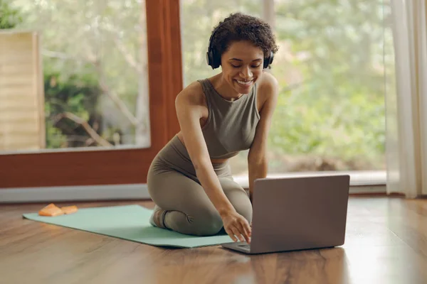 stock image Young sporty woman in headphones sitting on mat at home before doing fitness exercises