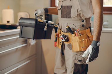 Ev mutfağında duran ve alet çantasını tutan profesyonel tamirciye yaklaş.