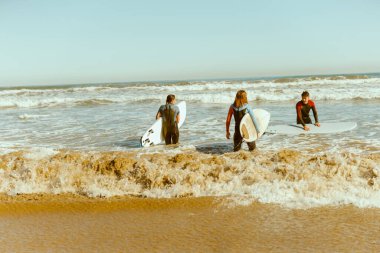 Sörf tahtası olan bir grup arkadaş dalgalar üzerinde sörf yapmak için okyanusa giriyorlar. Yüksek kalite fotoğraf 