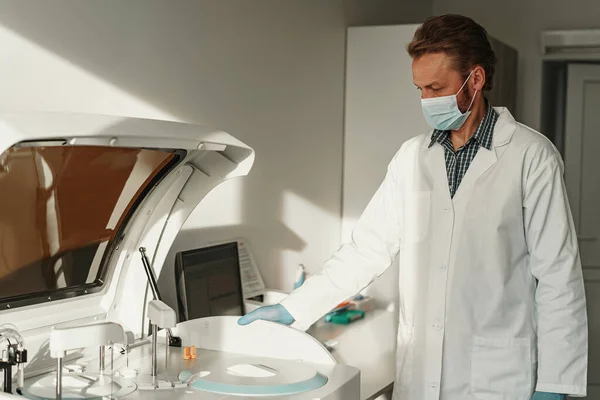 Male scientist in uniform and mask working in medical research laboratory. High quality photo