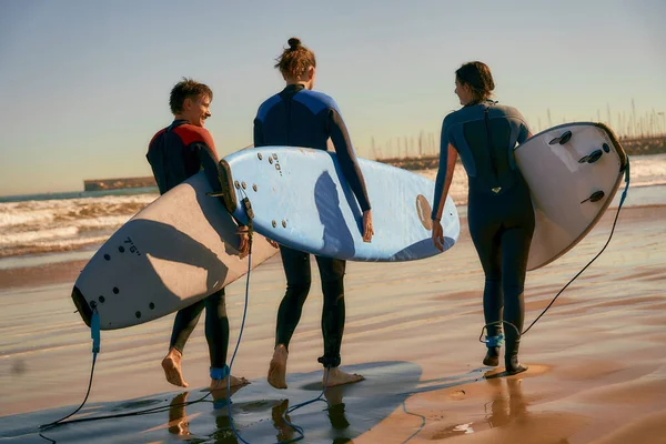 Widok Tyłu Grupy Przyjaciół Deskami Surfingowymi Kombinezonie Wchodzącymi Kierunku Oceanu — Zdjęcie stockowe