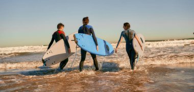 Sörf tahtası olan bir grup arkadaş dalgalar üzerinde sörf yapmak için okyanusa giriyorlar. Yüksek kalite fotoğraf 