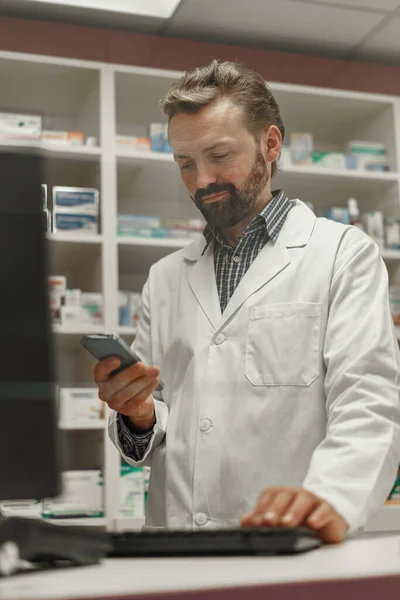 Male pharmacist using the computer and phone while working at the pharmacy. High quality photo