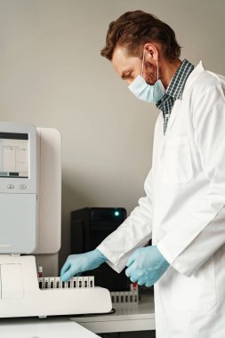 Tıbbi araştırma laboratuvarında çalışan üniformalı ve maskeli bir erkek bilim adamı. Yüksek kalite fotoğraf