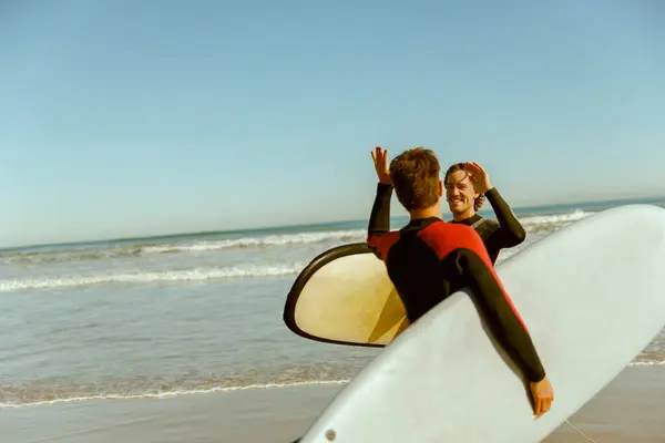 Surfer meets friend by waving hand while carrying surfboard on the beach. High quality photo