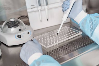 Üniformalı erkek bilim adamı tıbbi laboratuvarda biyokimyasal test analizi için mikro pipet kullanıyor. 