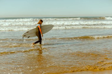 Dalgalar üzerinde sörf yaptıktan sonra sörf tahtasıyla denize giren dalgıç kılıklı mutlu bir kadın sörfçü.