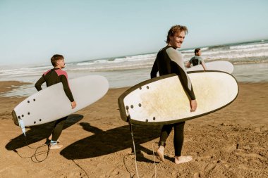 Sörf tahtası olan bir grup arkadaş dalgalar üzerinde sörf yapmak için okyanusa giriyorlar. Yüksek kalite fotoğraf 