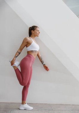 Eşofmanlı genç bayan sporcu dışarıda esniyor ve koşuya hazırlanıyor. Sağlıklı yaşam konsepti