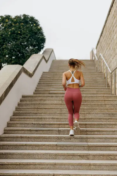 Back view of woman athlete in sportswear is jogging around city in early morning. Reaching the goal