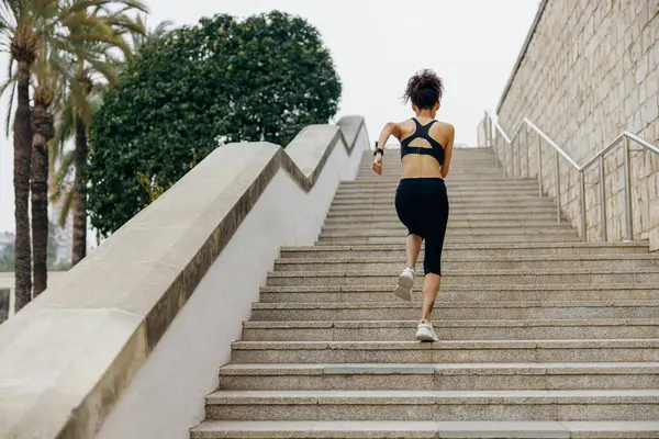 Spor giyimli aktif bayan sporcunun arka görüntüsü sabahın erken saatlerinde merdivenlerde koşuyor.