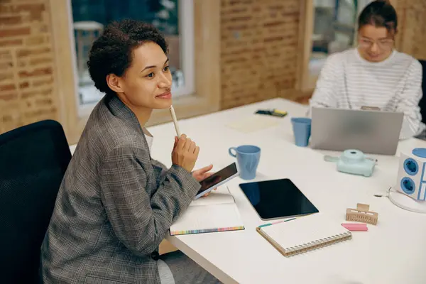 スタイリッシュな若い女性フリーランサーは同僚の近くに座っている現代オフィスで働いている間ノートを作っています — ストック写真