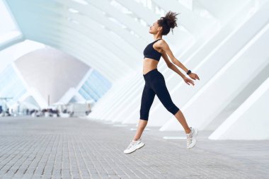 Bir kadın bir bacağı binanın önünde havaya sıçrıyor.