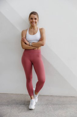 Spor kıyafetli gülümseyen kadın bina arkasında antreman yaptıktan sonra dinleniyor.