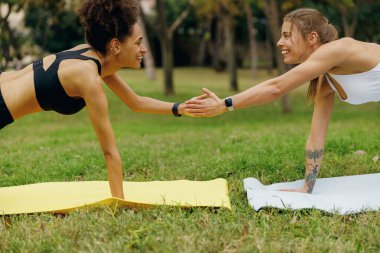 İki genç bayan arkadaş bir el parkta birbirlerini tutarken kalas egzersizi yapıyorlar.