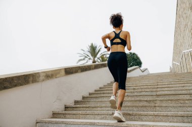 Spor giyimli aktif bayan sporcunun arka görüntüsü sabahın erken saatlerinde merdivenlerde koşuyor.