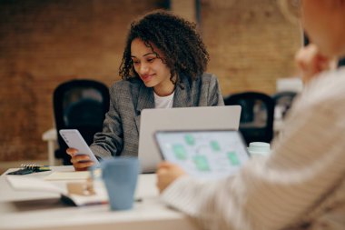Dijital tablet ve dizüstü bilgisayar üzerinde çalışırken açık ofiste oturan bir grup kadın yönetici