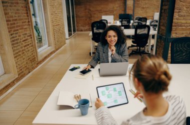 Bir grup kadın yönetici, bilgisayar ve dijital tablet üzerinde çalışırken açık modern ofiste oturuyorlar.