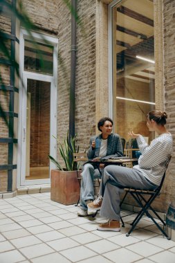 Gülümseyen kadın iş arkadaşları kafede otururken kahve içip sohbet ediyorlar.