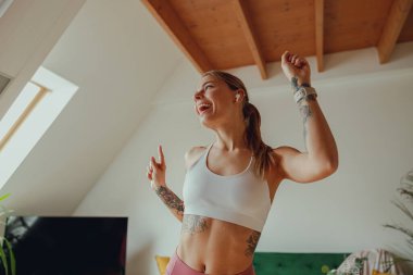 Oturma odasında kolları havada dans eden bir kadın var.