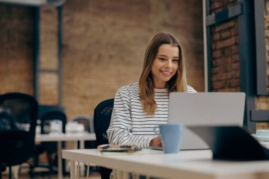 Genç bayan serbest çalışan, modern iş yerinde çalışırken dizüstü bilgisayarda çalışıyor.