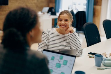 İki gülümseyen bayan meslektaşımız proje üzerinde çalışıyor ve ofiste dizüstü bilgisayar kullanıyorlar.