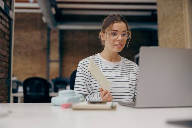 Ofisteki video konferansında iş arkadaşına bir şey gösteren gözlüklü kadın yönetici.
