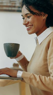 Gülümseyen bir kadın kahvesini düzenli bir masada içer, verimliliği ve rahatlığı rutiniyle harmanlar.
