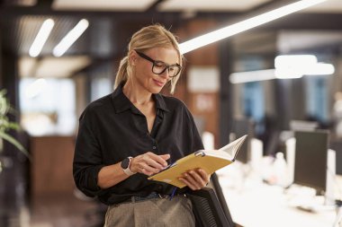 Modern bir çalışma alanında, şık, profesyonel bir kadın çalışırken dikkatle defteriyle meşgul olur.