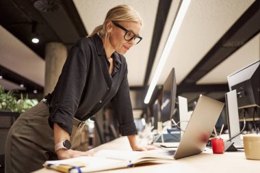 Kendini işine adamış profesyonel bir kadın, modern ofis ortamında çalışırken dizüstü bilgisayarıyla derinden ilgilenir.