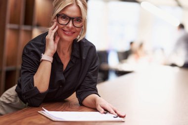 Profesyonel bir kadın, modern bir ofis masasında modern bir ortamda otururken tamamen işiyle meşguldür.