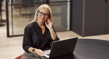 An ambitious and focused professional woman is using her laptop in a stylish, modern office environment clipart