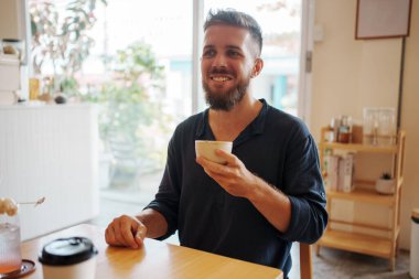 Sıcak bir kafede kahvesini yudumlayan neşeli bir adam, rahatlama ve neşe saçıyor.