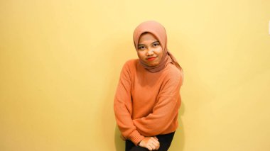 Turuncu arka planda sinirli yüz ifadesi olan Asyalı genç bir kadının stüdyo fotoğrafı. Genç kadın duygu yüz ifadesi portre konsepti