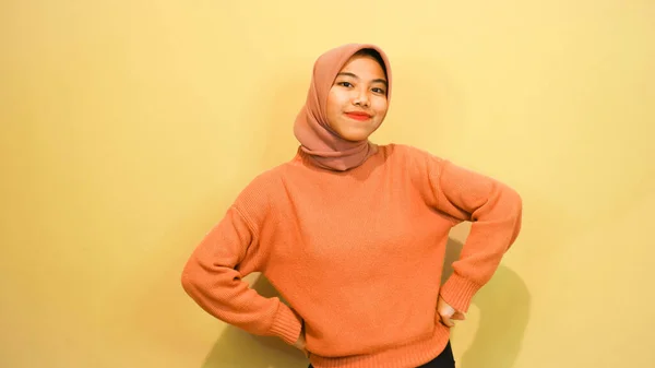 兴奋的亚洲穆斯林妇女穿着橙色毛衣 头戴头巾 指着旁边被橙色背景隔开的抄袭空间 — 图库照片