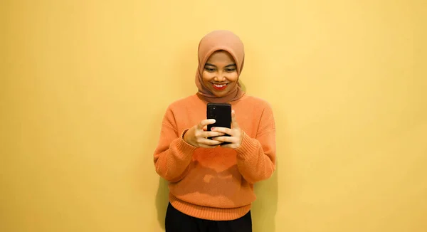年轻美丽的亚洲女人穿着橙色毛衣 用智能手机隔离橙色背景 — 图库照片