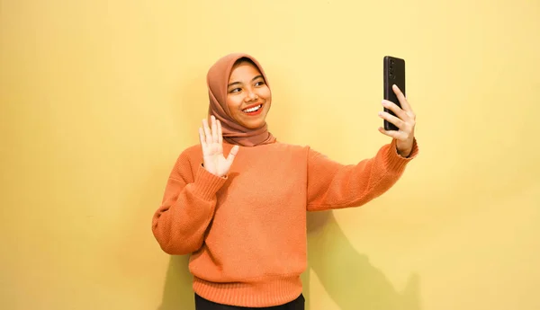 オレンジ色のセーターを着た若い美しいアジアの女性はオレンジの背景に隔離されたスマートフォンを使用 — ストック写真