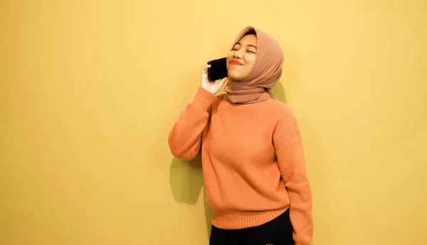 オレンジ色のセーターを着た若い美しいアジアの女性はオレンジの背景に隔離されたスマートフォンを使用 — ストック写真