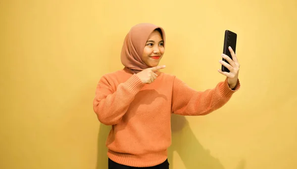 年轻美丽的亚洲女人穿着橙色毛衣 用智能手机隔离橙色背景 — 图库照片