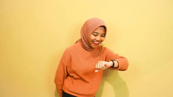 笑顔若いです女の子身に着けていますオレンジ色のセーター見ます彼女のスマートウォッチ隔離されました上のオレンジの背景 — ストック写真