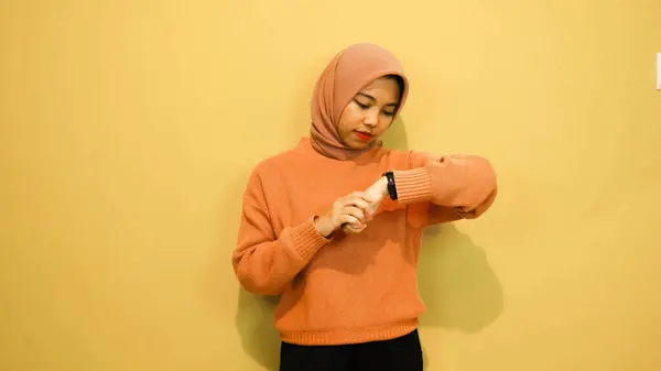 笑顔若いです女の子身に着けていますオレンジ色のセーター見ます彼女のスマートウォッチ隔離されました上のオレンジの背景 — ストック写真
