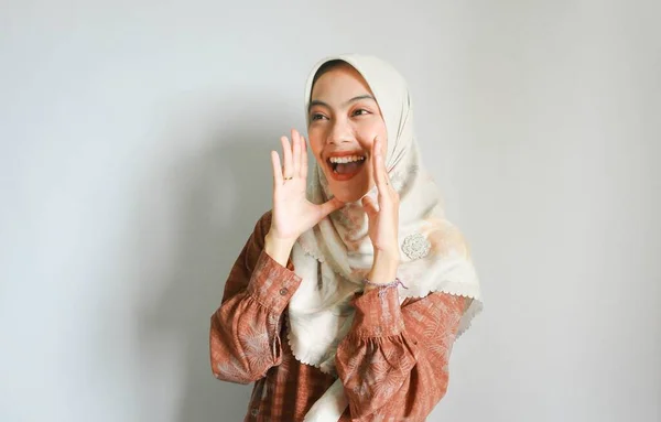 年轻美丽的亚洲穆斯林妇女头戴头巾大喊大叫 一只手捂着嘴 被白色背景隔开 传播概念 — 图库照片