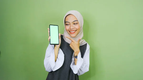 ヒジャーブを着たアジア系の若い女性が携帯電話の画面にコピースペースを見せています 緑の背景に隔離された — ストック写真
