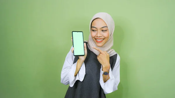 ヒジャーブを着たアジア系の若い女性が携帯電話の画面にコピースペースを見せています 緑の背景に隔離された — ストック写真
