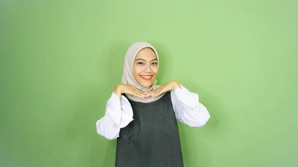 快乐的亚洲穆斯林女人 穿着休闲装 头戴头巾 指着旁边被绿色背景隔开的复制空间 — 图库照片